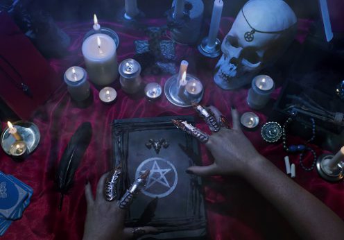 Witchcraft composition with witch's hands, satanic magic books, skull, candles, tarot cards, crystal and amulets. Halloween and occult concept, black magic ritual.
