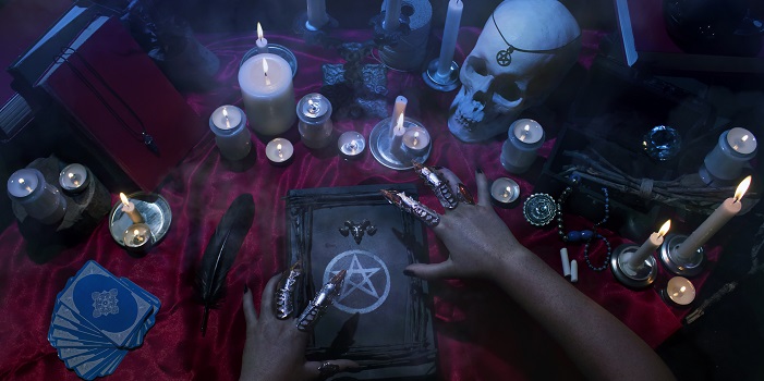 Witchcraft composition with witch's hands, satanic magic books, skull, candles, tarot cards, crystal and amulets. Halloween and occult concept, black magic ritual.